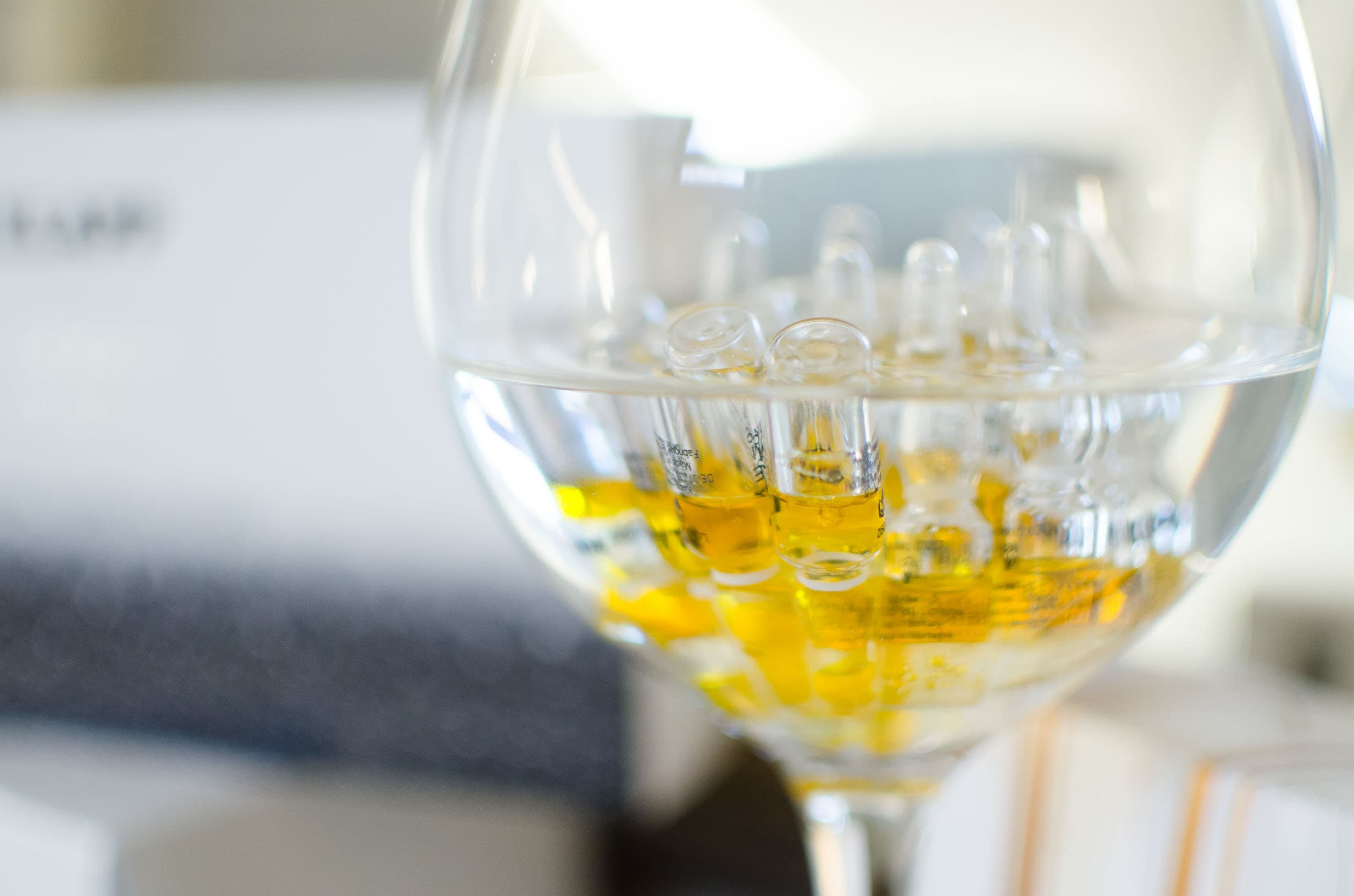 Stielglas mit Wasser, darin stehen kleine Glasampullen mit goldgelbem Inhalt